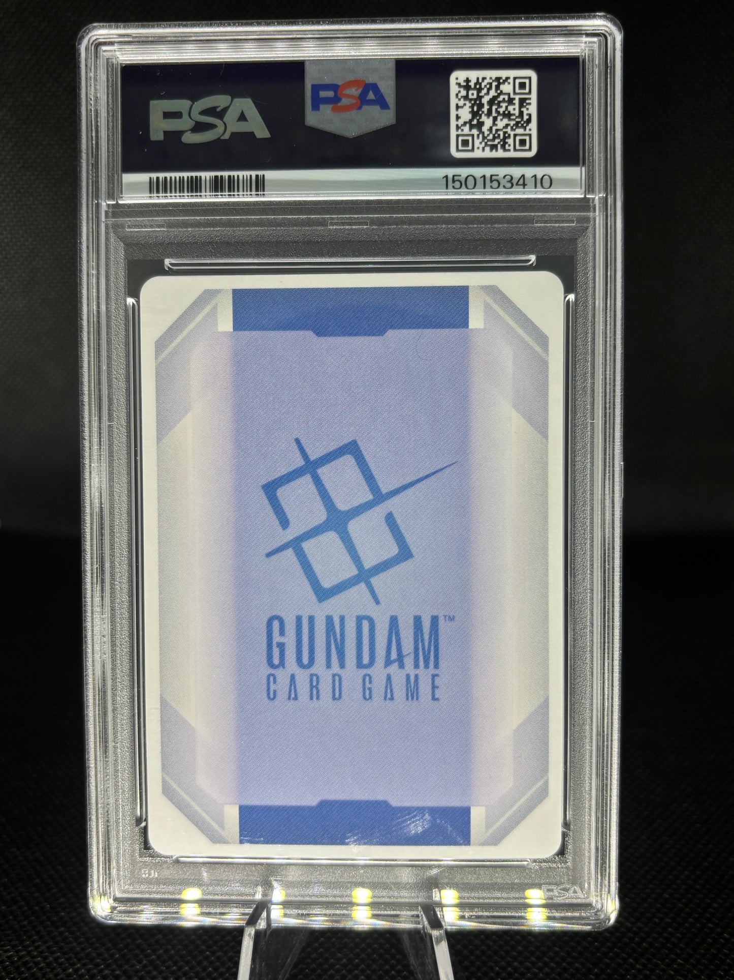 A PSA graded Gundam Card Game card sealed in a clear PSA slab, displayed on a stand against a dark background. The card features a light blue and white geometric design with the blue Gundam logo and text.