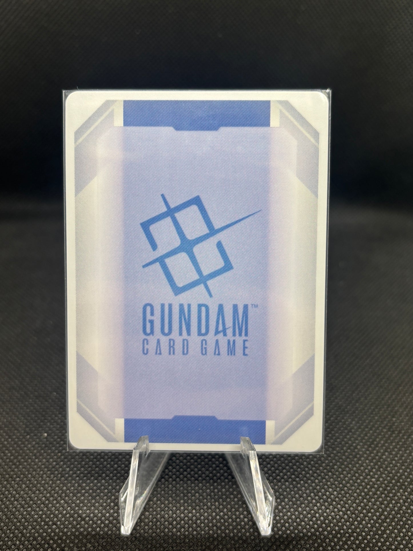 Gundam card game packaging with clear plastic holder on a dark textured background