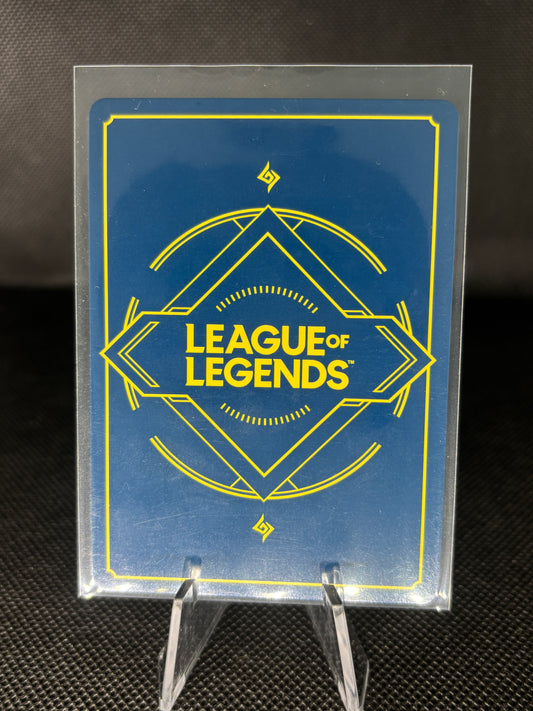 A blue and yellow League of Legends collectible card or sticker encased in a clear protective plastic sleeve, displayed on a clear stand against a dark textured background.