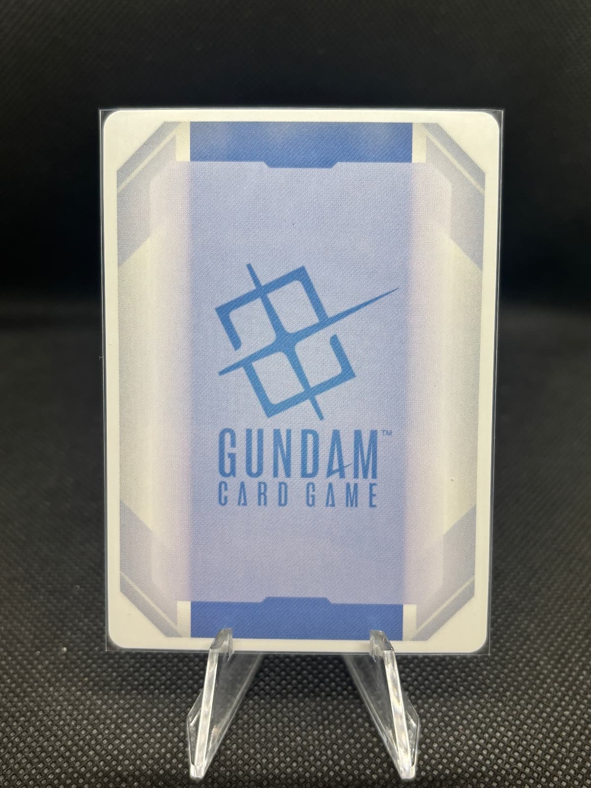 Gundam card game packaging with clear lid on a dark textured background