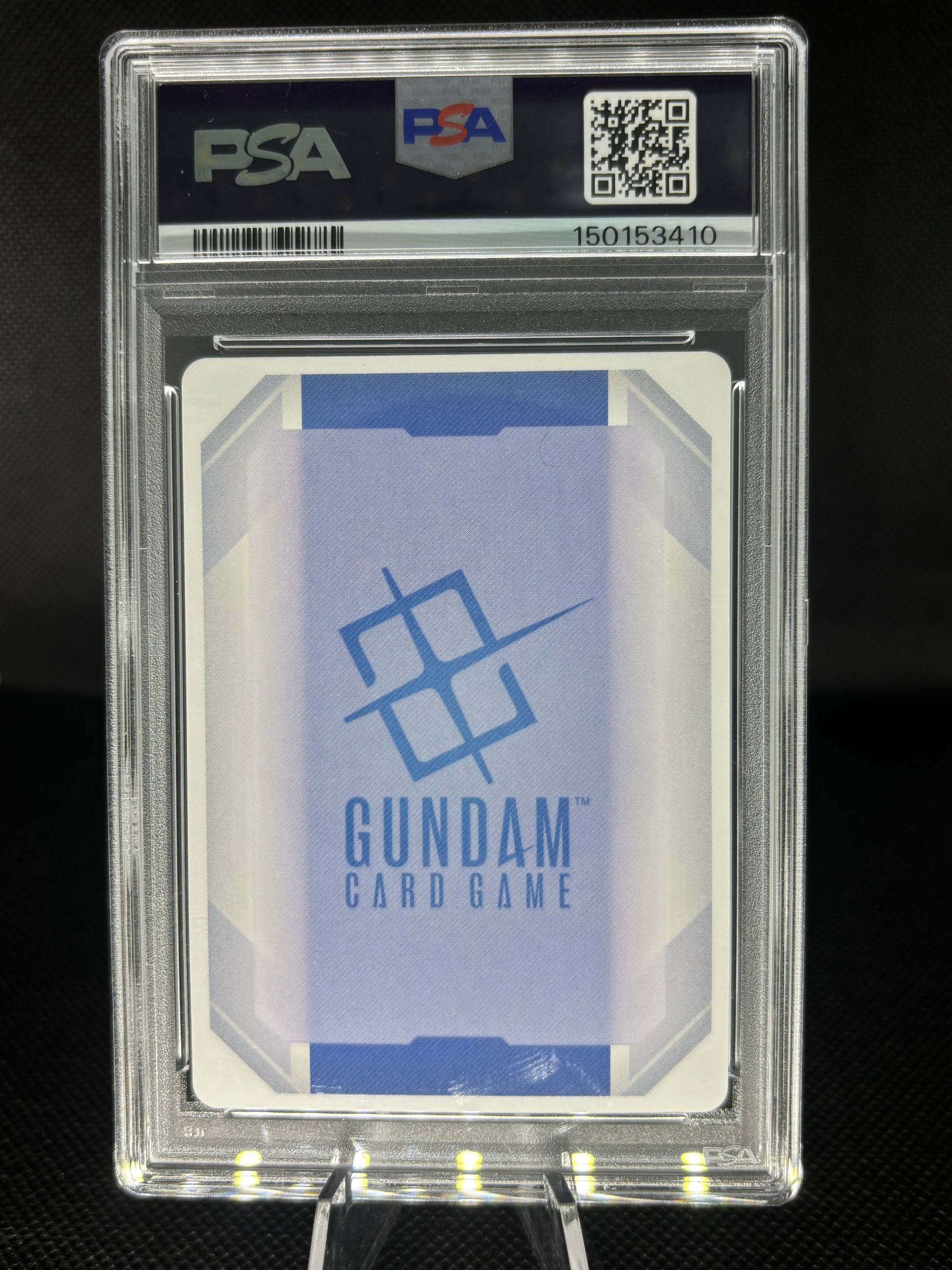 A PSA graded Gundam Card Game card sealed in a clear PSA slab, displayed on a stand against a dark background. The card features a light blue and white geometric design with the blue Gundam logo and text.